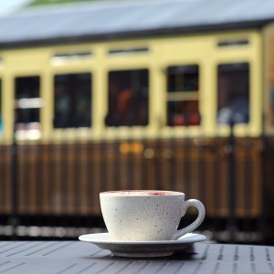 Cup of coffee on table with vintage train in the background.