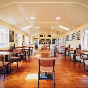 Cozy, well-lit café interior with wooden floor, tables, and chairs, decorated with framed art on cream walls.