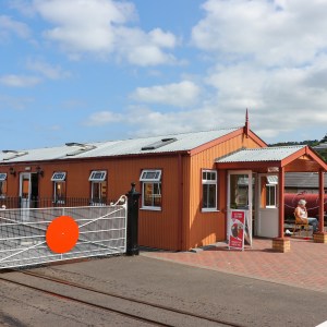 Orange building with metal roof, fenced railway crossing, and people sitting outside on a sunny day.