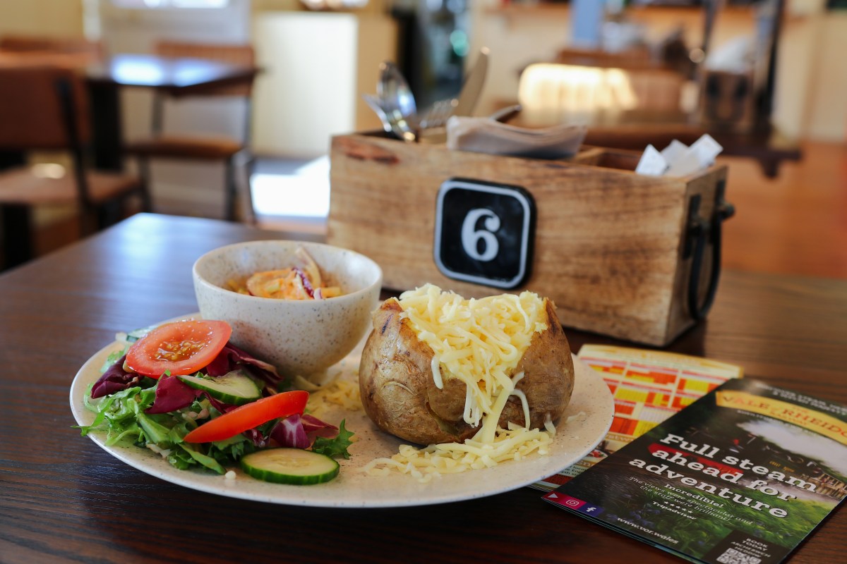 Plate with salad, baked potato, and cheese beside a bowl and wooden box on a table with flyers.