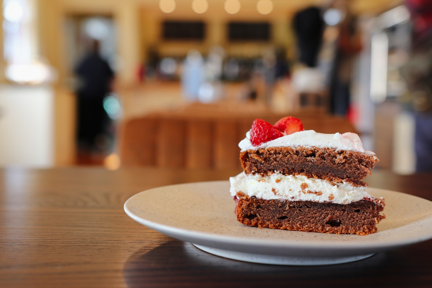 Slice of chocolate cake with cream and strawberries on a plate in a cafe.