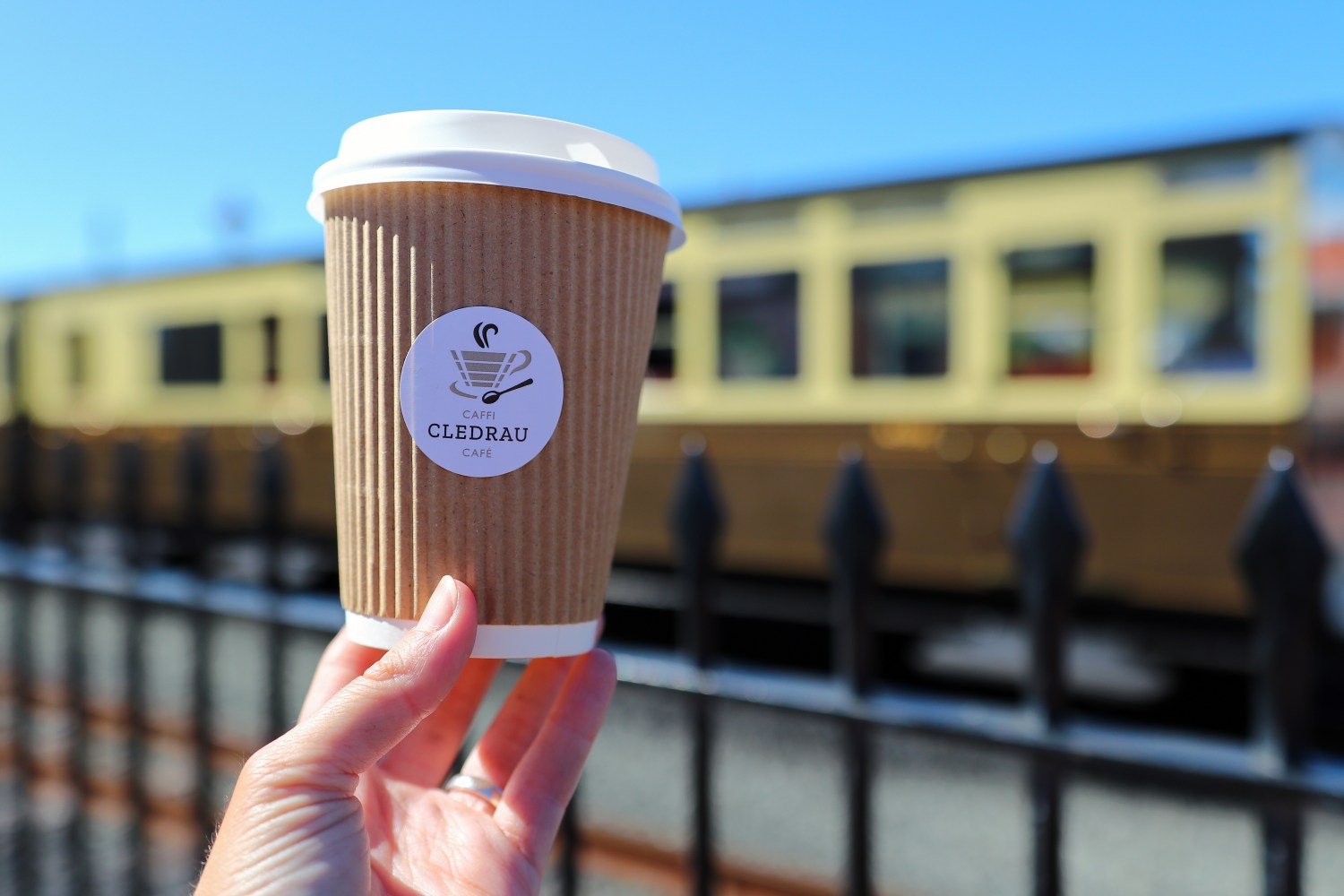 Hand holding a coffee cup with a train in the background.