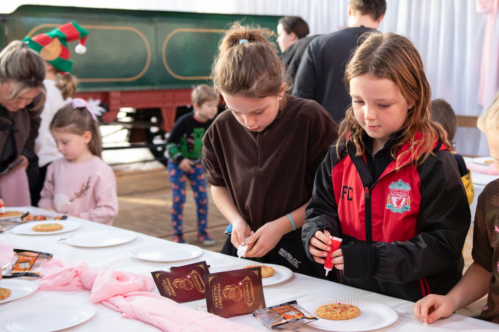 Children decorate cookies at a table, wearing casual clothes and holiday-themed attire.