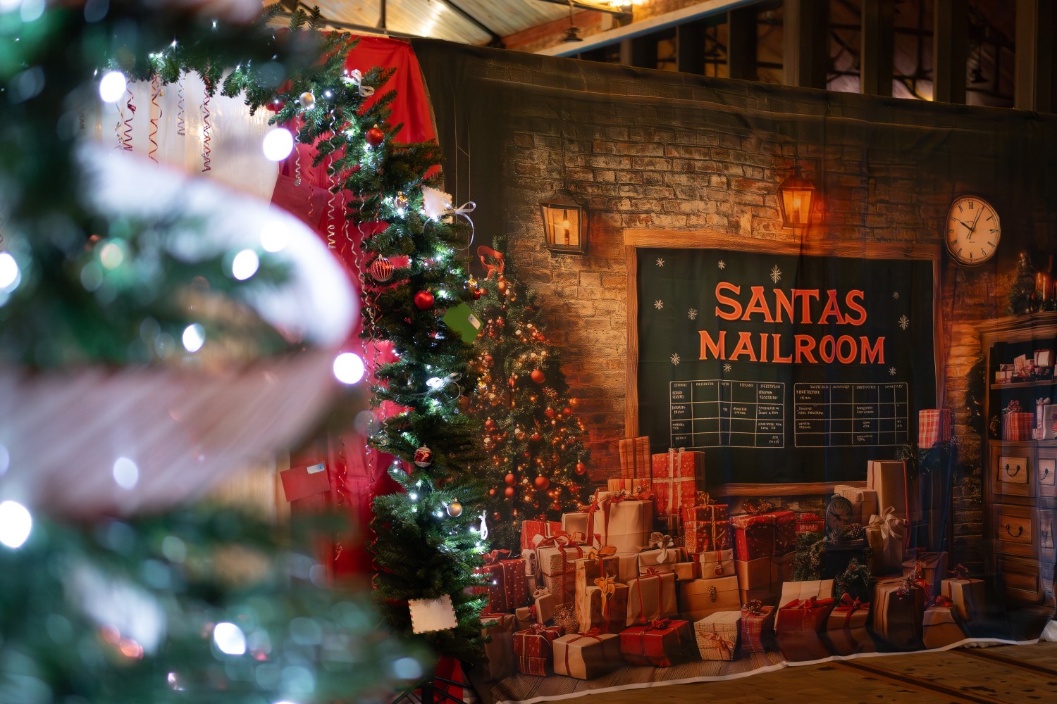 Festive room with decorated Christmas trees and a 'Santas Mailroom' sign, surrounded by presents.