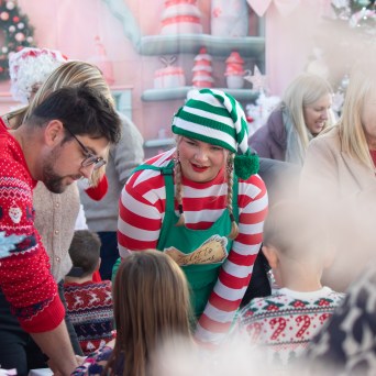 Festive gathering with people in holiday sweaters and an elf costume at a decorated Christmas event.