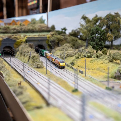 Miniature train set with trains on tracks, tunnels, and lush landscape background.