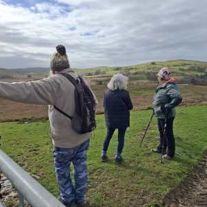 Three people standing on a hill, overlooking a green and brown landscape.