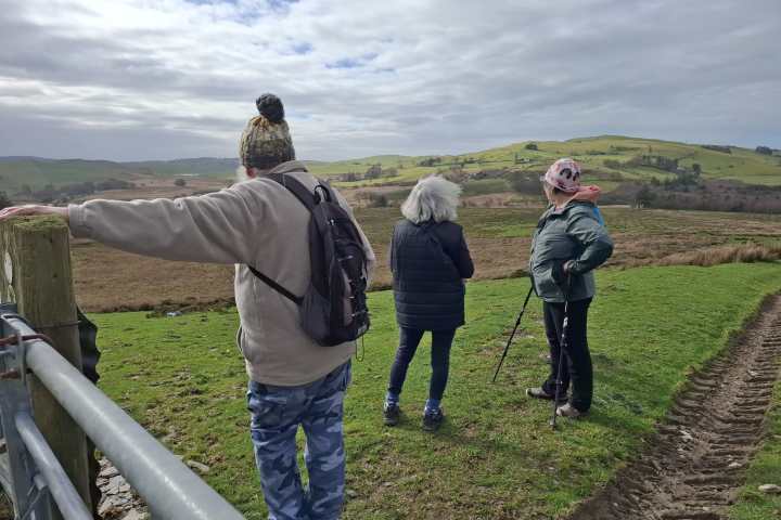 Three people standing on a hill, overlooking a green and brown landscape.