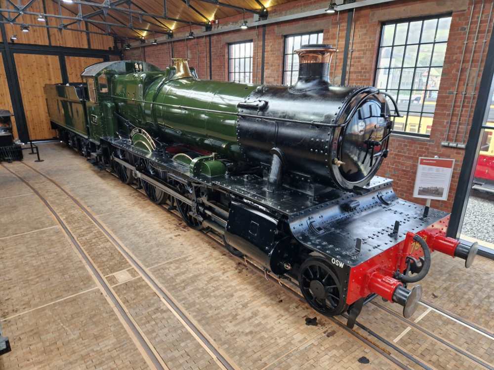 A vintage green steam locomotive displayed indoors on wooden tracks.