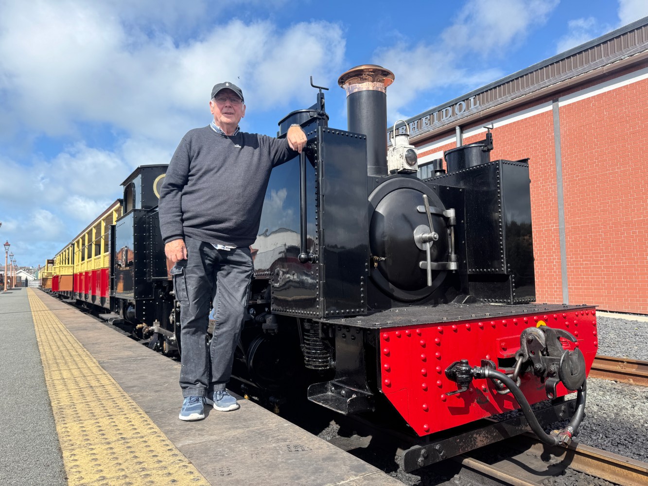 Man standing beside a vintage steam train on a sunny day.