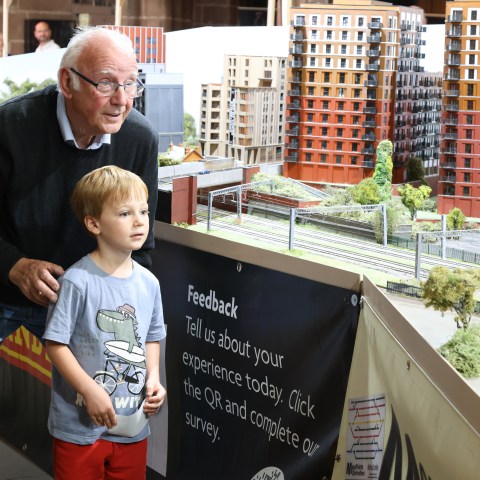 Elderly man and boy observing a detailed model train exhibit with miniature buildings and greenery.