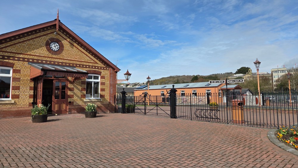 Entrance to a vintage railway station with brick building and gates.