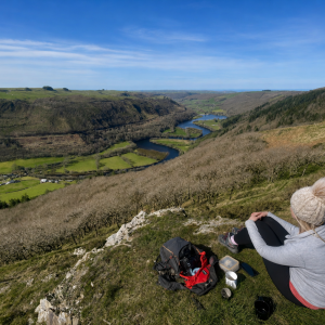 Person sitting on a hill, overlooking a winding river and valley.