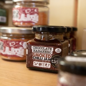 Jars of assorted smoked chilli jam on a wooden shelf.