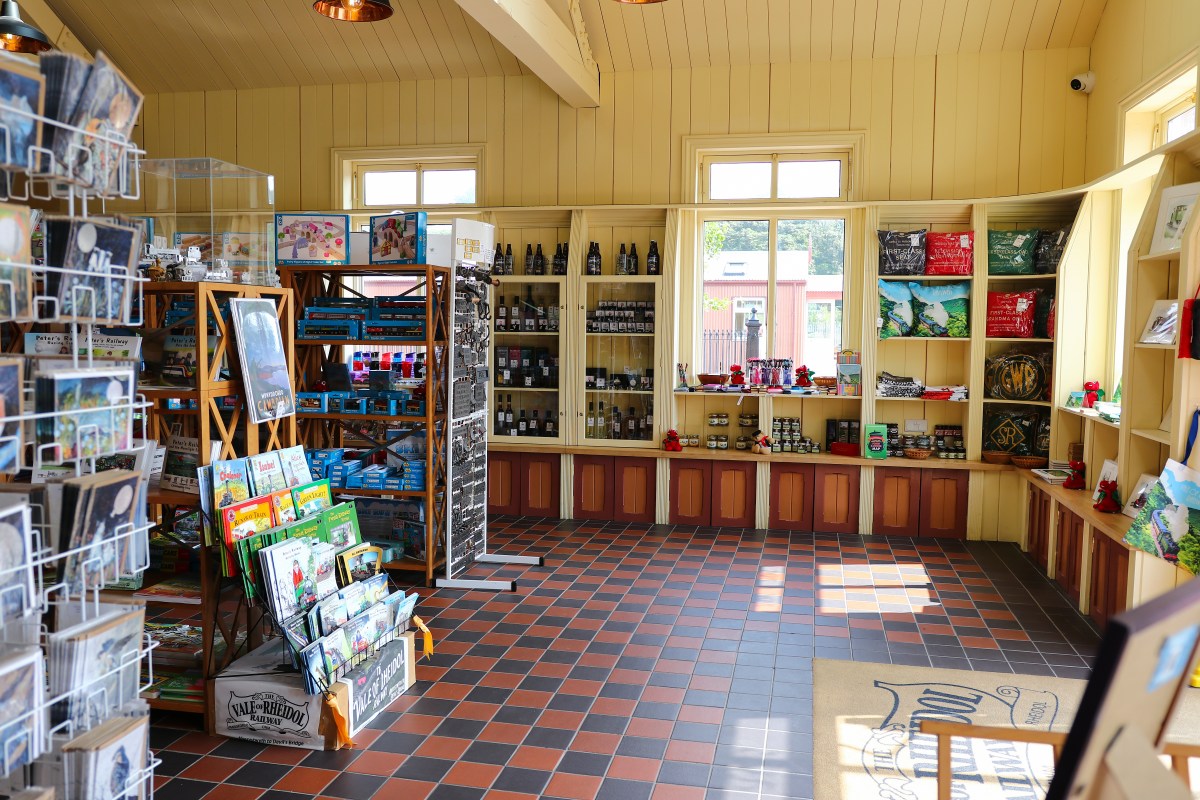 Gift shop with shelves of souvenirs, postcards, and books, lit by sunlight through windows.