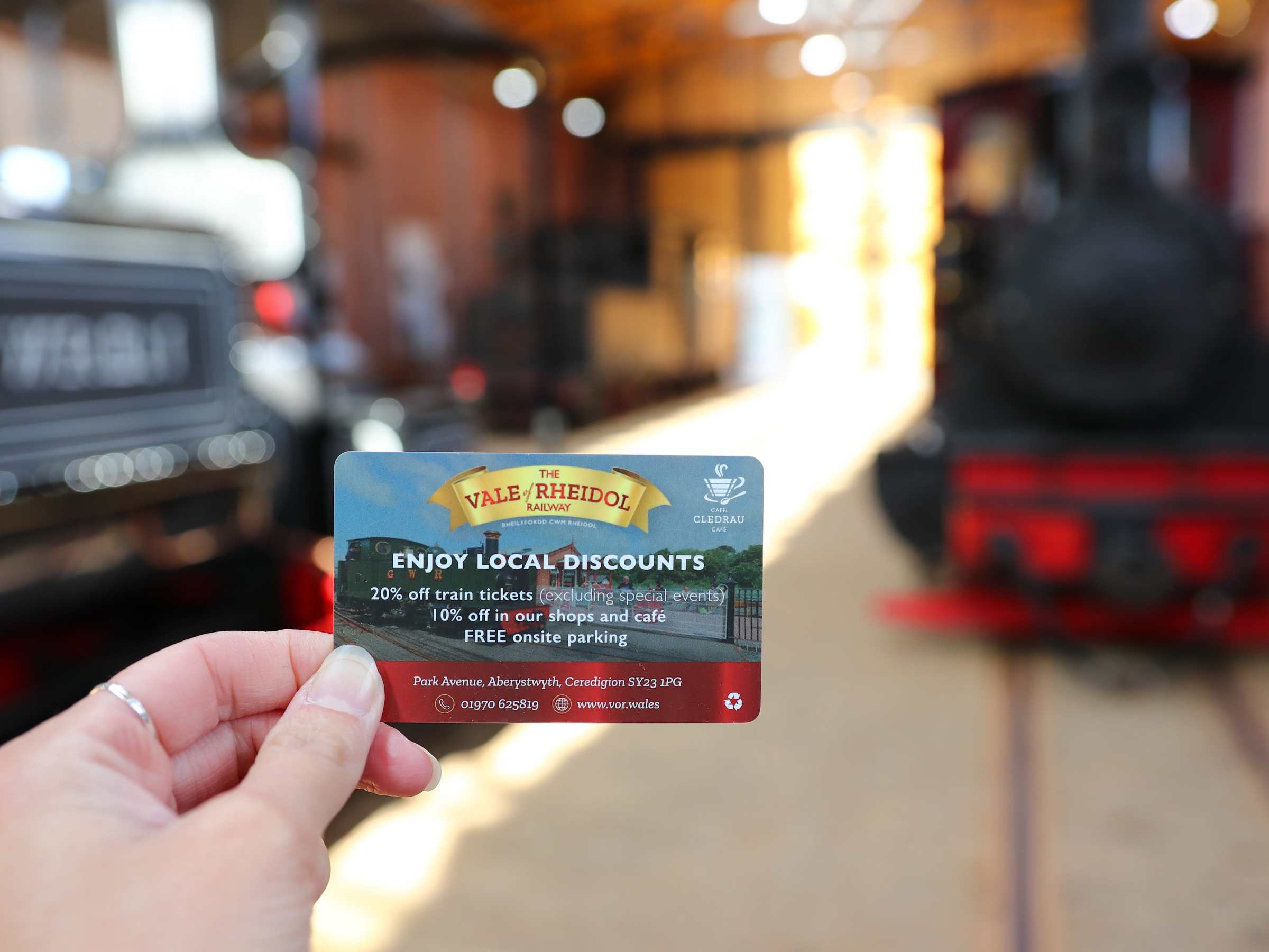 Hand holding a discount card in front of steam trains in a museum.