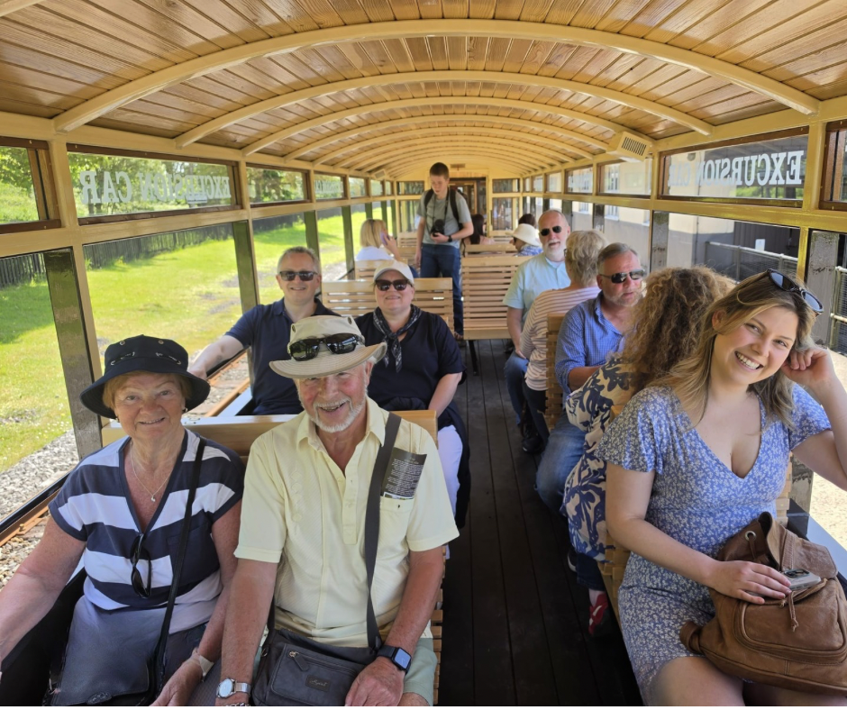 Group of smiling people sitting inside an open-air excursion train car.