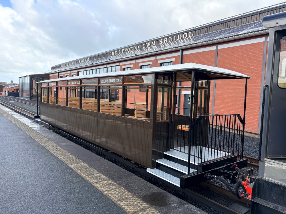 Historic railcar at station, with wooden seats and classic design.