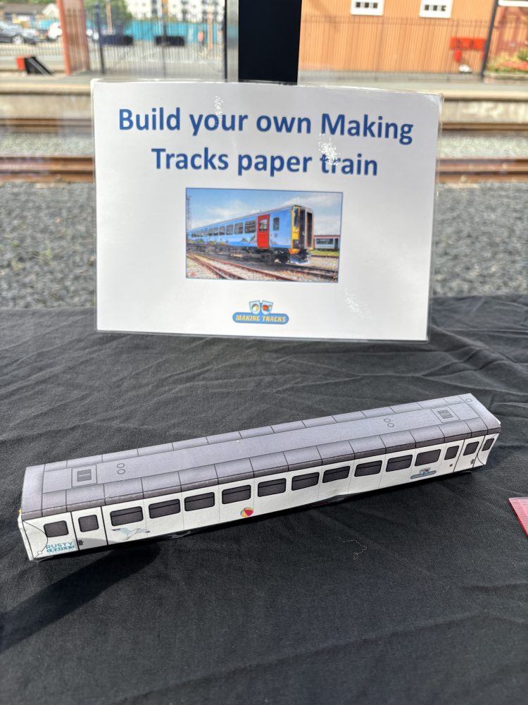 Paper model train next to sign: 'Build your own Making Tracks paper train.'