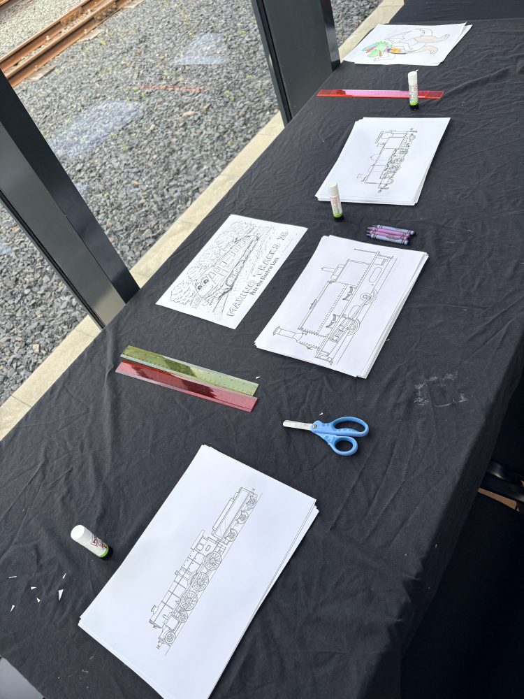 Table with coloring sheets, crayons, scissors, and glue on a black tablecloth.