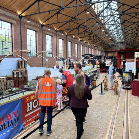 People viewing model train exhibit in large hall with glass ceiling.