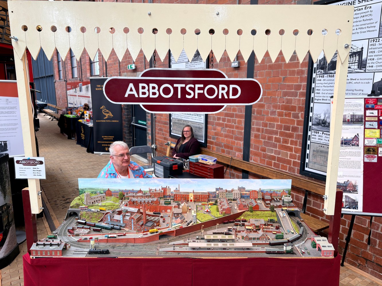Model train display labeled 'Abbotsford' with two people seated behind it.