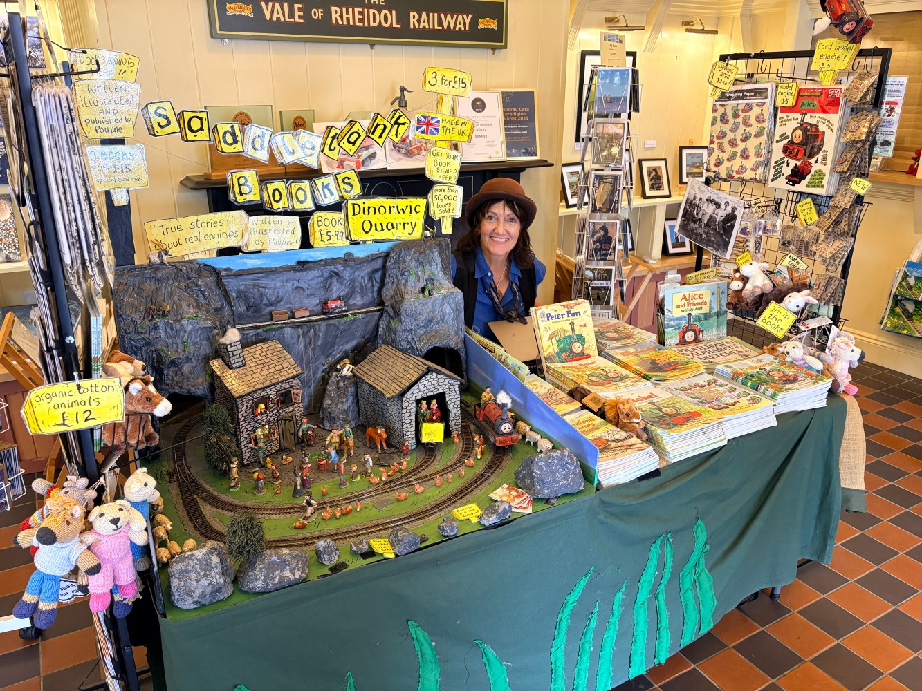 Woman in hat at book and toy stall with train set display.