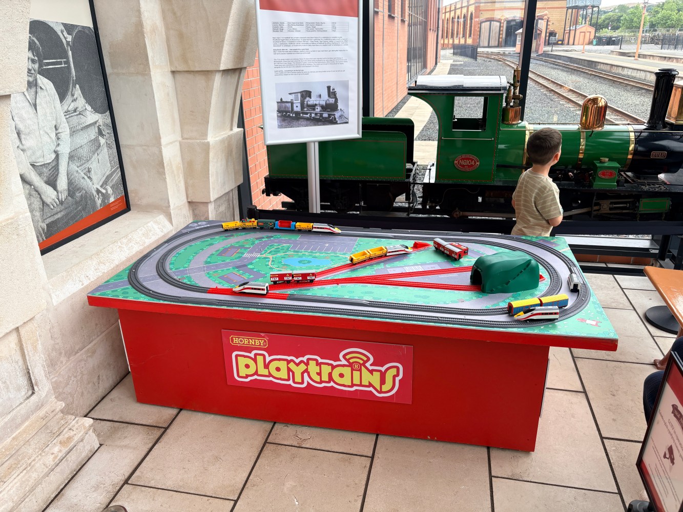 Child near toy train display with tracks, trains, and playtable.